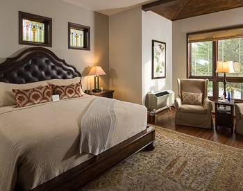 Wood platform bed with leather Headboard lined in brown wood. One tan high back chair and an view of the mountains out the window.